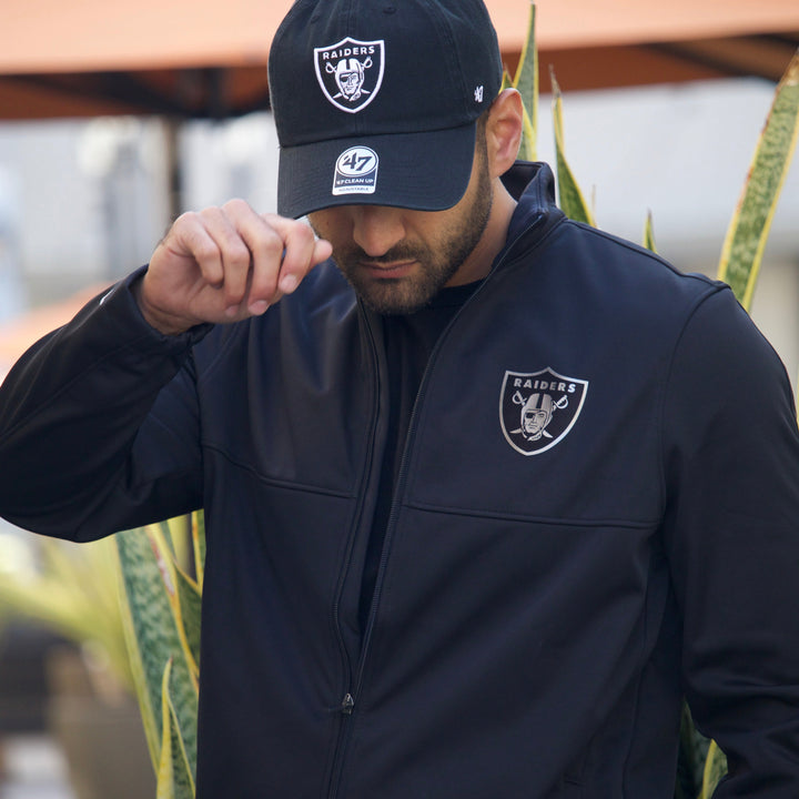 Person wearing a dark las vegas raiders jacket and raiders cap, standing outdoors.